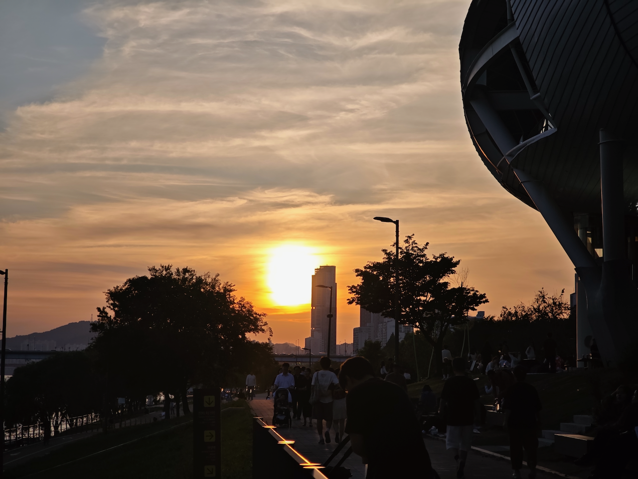太阳正落在汉江桥的下面，江边圆形浮岛咖啡的剪影立在画面右侧